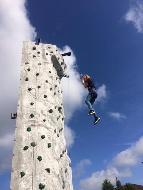 Climber being lowered from the top of the grey wall on the blue belay line against a blue sky