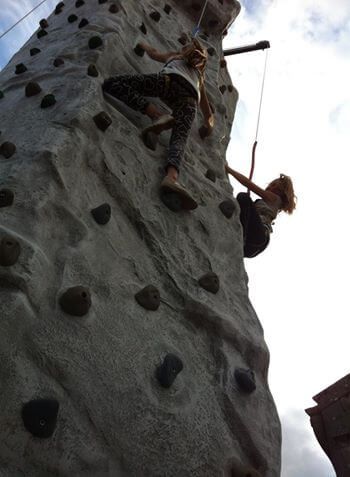 Two children climbing different faces of the grey rock-effect wall against a cloudy sky